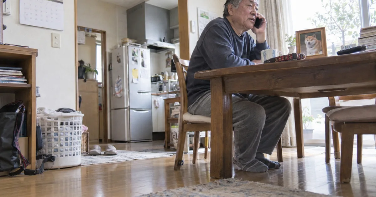 柴犬の写真と首輪を前に電話をかける60代の男性
